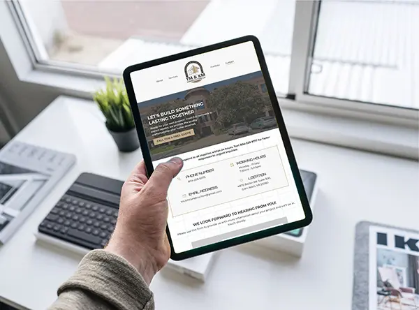 A hand holding a tablet displaying the contact page of the TM & KM Construction website. The screen shows contact information, including phone number, email, and location in Glen Allen, VA.